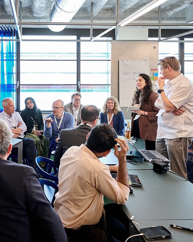 Fachleute diskutieren bei einem Workshop an einem Tisch, im Hintergrund ein Flipchart mit „Wet Barrier Coating“