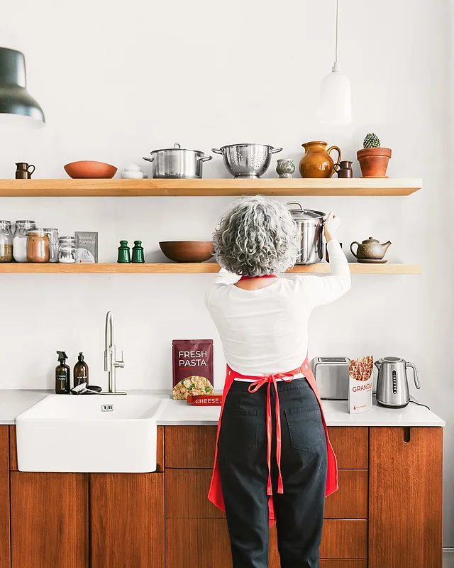 Frau greift in der Küche nach einem Topf, davor Papierverpackungen für Pasta und Granola von Felix Schoeller