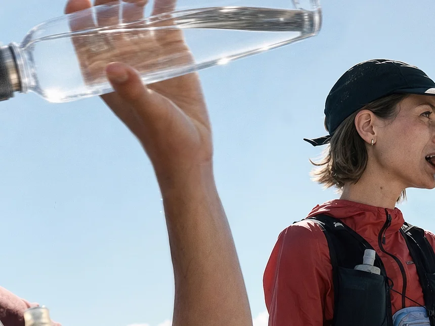Wanderer trinkt Wasser, daneben isst eine Frau im Gebirge einen Protein-Riegel aus Papierverpackung von Felix Schoeller